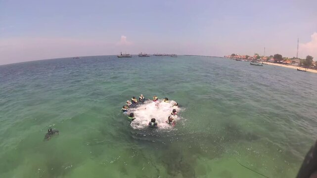 "Aerial view of a group of snorkelers in life jackets forming a circle and splashing water in the clear turquoise sea near Gili Ketapang beach."