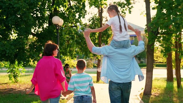 Happy parents, children, son mother, daughter father shoulders, walk together, enjoying sun nature. Family strolling in park, happy people. Family picnic with child in outdoors. Dad mom son travel