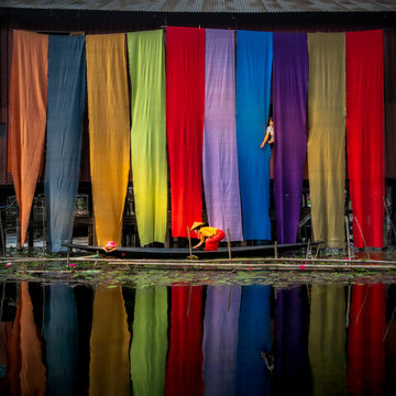 Inle Lake, Myanmar - 14 November 2019: View of vibrant fabrics casting colorful reflections on the still waters. Three generational family involved in the dyeing cloth trade.