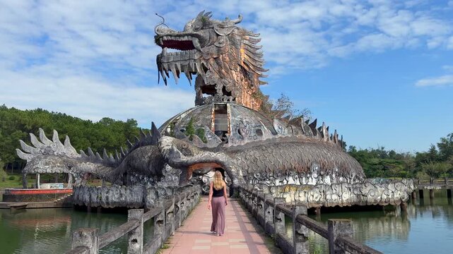 Woman walking toward giant dragon structure at abandoned water park in Hue, Vietnam. Unique travel destination and urban exploration landmark in Southeast Asia.