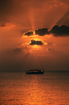 A Maldivian Dhoni boat passing by the sunset.
