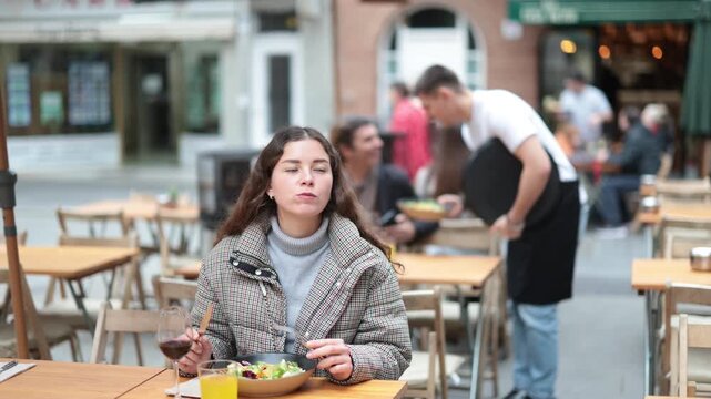 On open area of cafe, girl in restaurant eating salad. Single client sits at table, eats and enjoys views of ancient European city around.