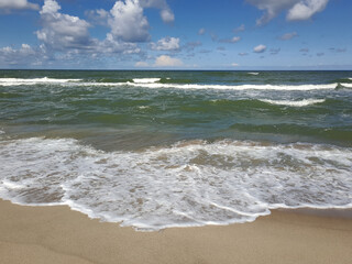 Sandy beach with turquoise waves and white foam under blue sky