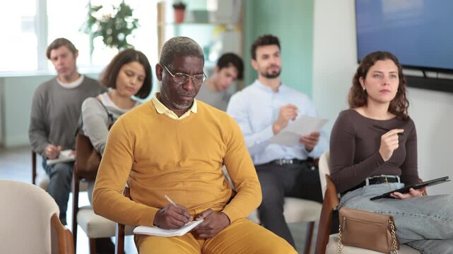 Students of different ages listen attentively to the teacher and take notes in notebooks during a lecture at the learning center. Language course. High quality 4k footage