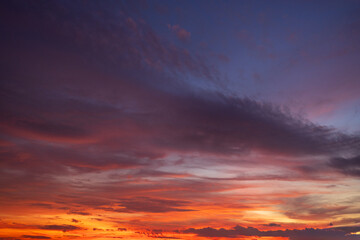 Obraz premium Dramatic sunset sky with vibrant orange and purple clouds at twilight,A breathtaking panoramic view of a colorful sunset sky featuring a mix of fiery orange, deep purple, and blue hues.