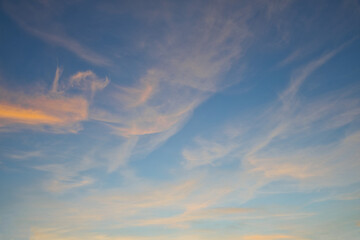 Soft orange clouds illuminated by the setting sun against a blue evening sky. Peaceful sunset atmosphere with warm light and natural color contrast. © jarizPJ