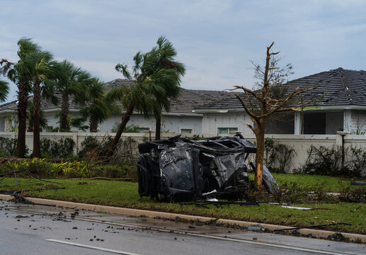 Palm Beach Gardens, United States - 09 October 2024: View of an overturned vehicle amidst debris-strewn lawns, with damaged palm trees and houses hinting at a recent storm's fury.