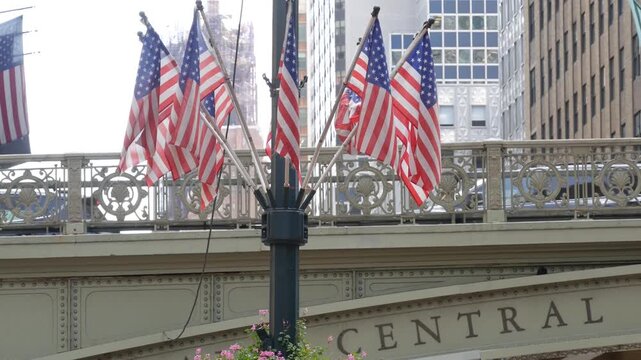 American flags near Grand Central Terminal on 42 street, New York City, Manhattan Midtown. Bridge to railway building, urban architecture in United States. Public railroad transport junction.