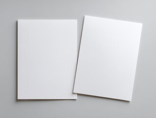 Two blank white sheets of paper placed on a smooth grey surface with one slightly tilted, highlighting clean minimalist stationery concept for design or presentation