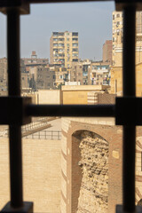 Urban view of residential buildings through barred window in Cairo with historic stone wall foreground