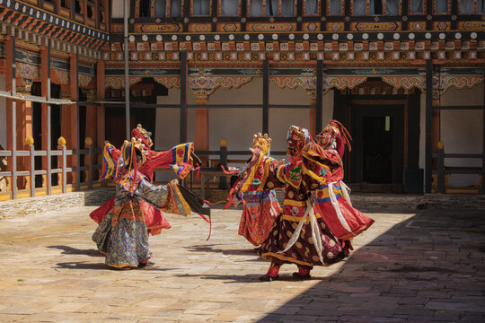 Jakar Dzong, Bhutan - 24 September 2025: View of dancers in vibrant costumes and masks performing a traditional dance within the courtyard of the ancient fortress, bathed in the warm light.