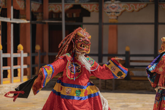 Jakar Dzong, Bhutan - 24 September 2025: View of a vibrant, masked dancer in red robes, performing a traditional ritual amidst the Dzong's ancient walls.
