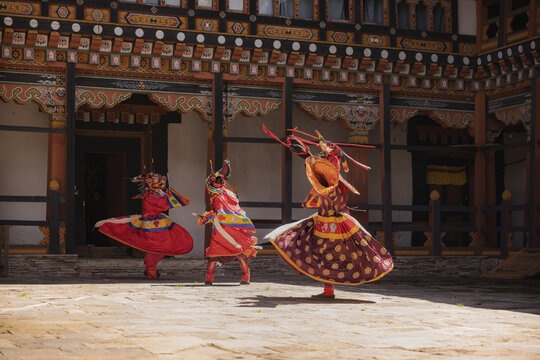 Jakar Dzong, Bhutan - 24 September 2025: View of dancers in vibrant traditional attire performing a ritual dance against the backdrop of ornate architectural details and sunlit courtyard stones.