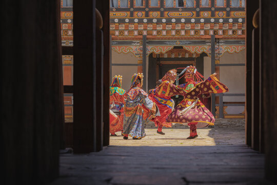 Jakar Dzong, Bhutan - 24 September 2025: View of dancers adorned in vibrant, patterned costumes, swirling and leaping within the ornately decorated courtyard, framed by stone archways.
