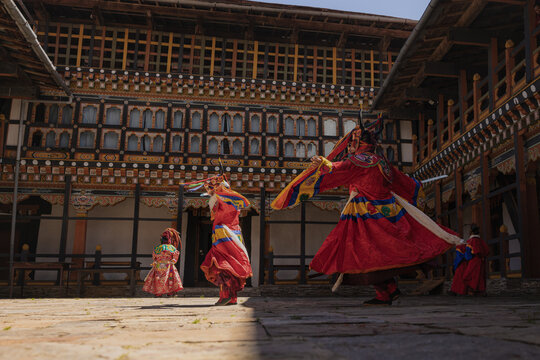 Jakar Dzong, Bhutan - 24 September 2025: View of dancers in vibrant red costumes twirling against the backdrop of the ancient fortress, its intricate windows casting long shadows across the courtyard.