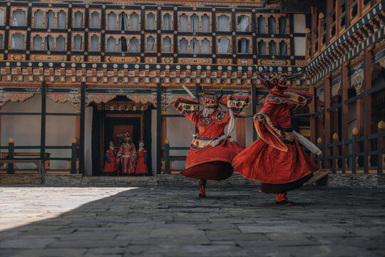 Jakar Dzong, Bhutan - 24 September 2025: View of masked dancers in vibrant red robes gracefully move across the stone courtyard, framed by the ornate architecture of the dzong.