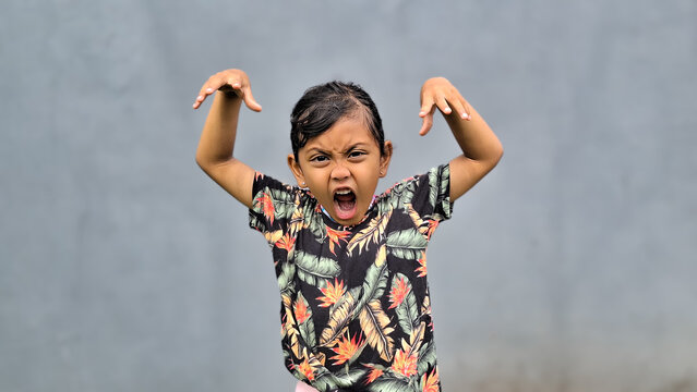 Cute Asian child is making a playful, roaring gesture with both hands raised on grey background isolated. Little girl with beach theme clothes expression to scare others.