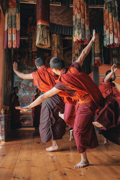 Jakar Dzong, Bhutan - 24 September 2025: View of monks in vibrant maroon robes gracefully dancing in a traditional hall, under ornate tapestries and intricate wall paintings.