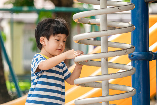 A cute and cheerful little Asian boy as he plays on an outdoor playground. The kid is laughing heartily while enjoying the activities in a public park, a genuine moment of happy childhood