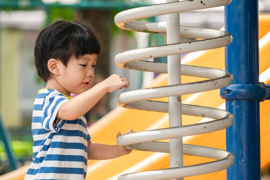 A cute and cheerful little Asian boy as he plays on an outdoor playground. The kid is laughing heartily while enjoying the activities in a public park, a genuine moment of happy childhood