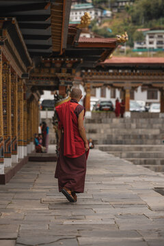 Thimphu, Bhutan - 28 September 2025: View of a monk in vibrant red robes walks along the stone path at Tashichho Dzong, where the ancient architecture meets the serene backdrop of the city.