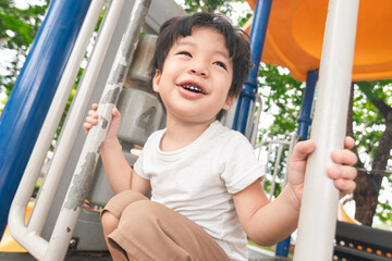 Obraz premium A cute and cheerful little Asian boy as he plays on an outdoor playground. The kid is laughing heartily while enjoying the activities in a public park, a genuine moment of happy childhood