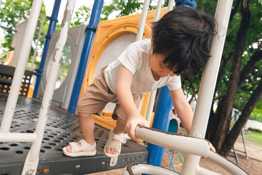 A cute and cheerful little Asian boy as he plays on an outdoor playground. The kid is laughing heartily while enjoying the activities in a public park, a genuine moment of happy childhood