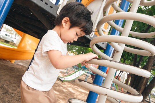 A cute and cheerful little Asian boy as he plays on an outdoor playground. The kid is laughing heartily while enjoying the activities in a public park, a genuine moment of happy childhood