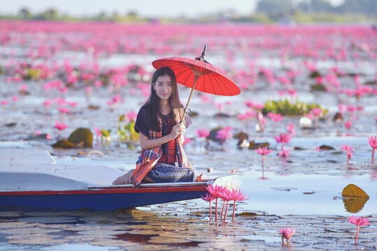 Young woman sitting in a boat holding a traditional parasol looking at the view, Red Lotus Sea (Talay Bua Daeng), Udon Thani, Northeast Thailand, Thailand