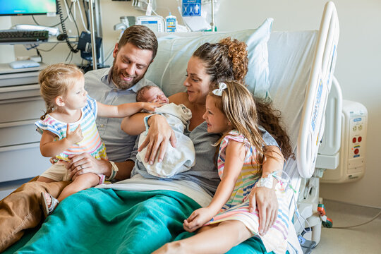 Woman sitting in a hospital bed with her husband and two children holding her newborn son