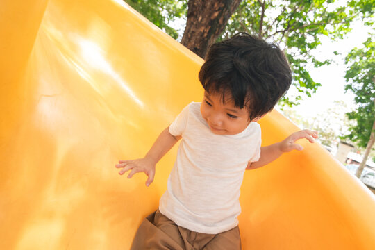 A portrait of a cute and cheerful little Asian boy as he plays on an outdoor playground. The kid is laughing heartily as they enjoy the Slide in a public park, a genuine moment of happy childhood.