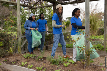 African American volunteers wearing blue tees holding green bags cleaning garden beds under pergola