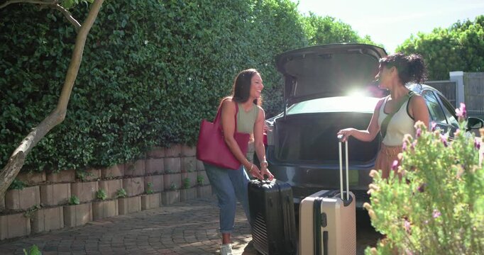 Diverse female friends pulling black and beige suitcases from trunk on driveway preparing for trip