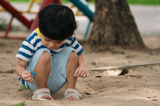 A portrait of a cute and cheerful little Asian boy as he plays on an outdoor playground. The kid is laughing heartily as they enjoy the sand in a public park, a genuine moment of happy childhood.