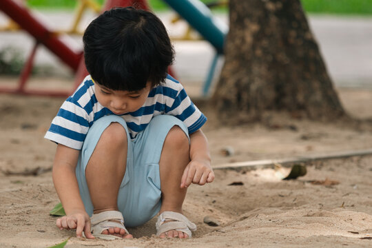 A portrait of a cute and cheerful little Asian boy as he plays on an outdoor playground. The kid is laughing heartily as they enjoy the sand in a public park, a genuine moment of happy childhood.
