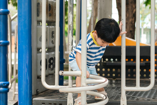 A cute and cheerful little Asian boy as he plays on an outdoor playground. The kid is laughing heartily while enjoying the activities in a public park, a genuine moment of happy childhood