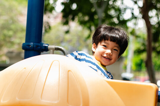 A cute and cheerful little Asian boy as he plays on an outdoor playground. The kid is laughing heartily while enjoying the activities in a public park, a genuine moment of happy childhood