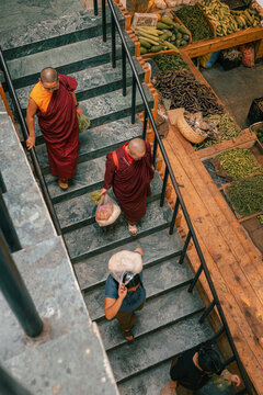 Thimphu, Bhutan - 27 September 2025: View of monks descending stone steps near vibrant market stalls overflowing with greens and produce, a scene of spiritual serenity amidst bustling commerce.