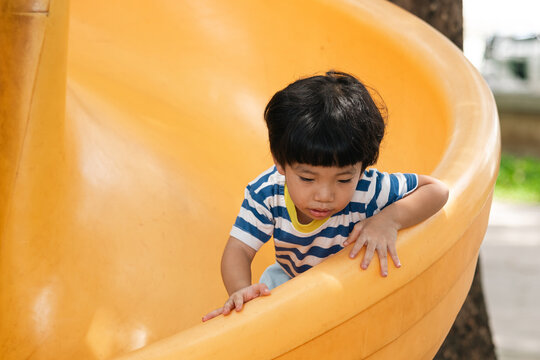 A portrait of a cute and cheerful little Asian boy as he plays on an outdoor playground. The kid is laughing heartily as they enjoy the Slide in a public park, a genuine moment of happy childhood.