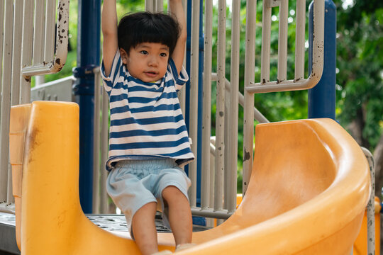 A portrait of a cute and cheerful little Asian boy as he plays on an outdoor playground. The kid is laughing heartily as they enjoy the Slide in a public park, a genuine moment of happy childhood.