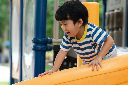 A portrait of a cute and cheerful little Asian boy as he plays on an outdoor playground. The kid is laughing heartily as they enjoy the Slide in a public park, a genuine moment of happy childhood.