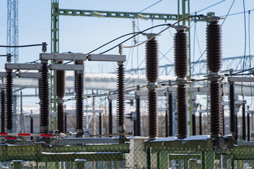 Electric transmission substation with porcelain insulator columns and switching hardware, metal structures and power lines under clear sky, industrial energy background