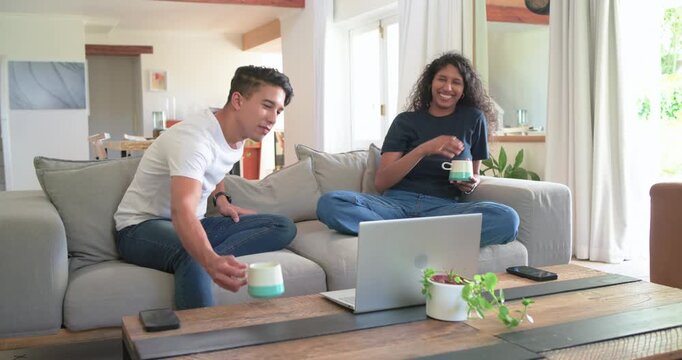 African American couple laughing, pointing at laptop, sipping mugs and reacting to content at home