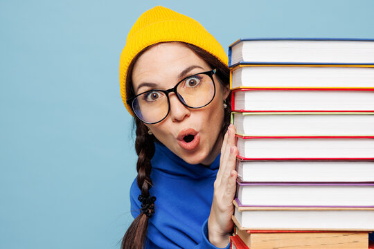 Young fun shocked amazed happy smart woman reader student she wear casual clothes hold stand behind stack of books isolated on pastel plain light blue color background. High college lifestyle concept.