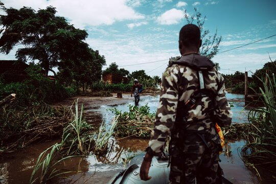 Manhica, Mozambique - 22 January 2026: View of a soldier's back as he wades through murky floodwaters, a scene of resilience amidst nature's powerful display.