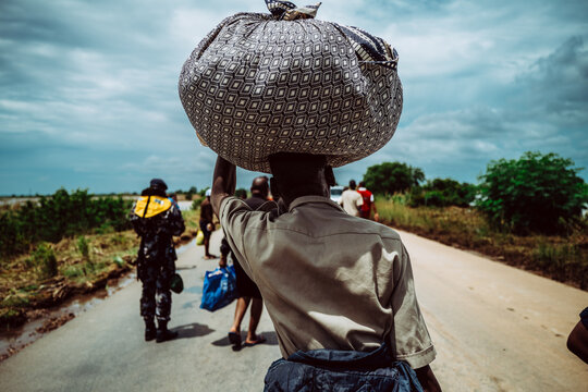 Manhica, Mozambique - 22 January 2026: View of a person carrying a large bundle on their head along a road under a bright, cloudy sky.