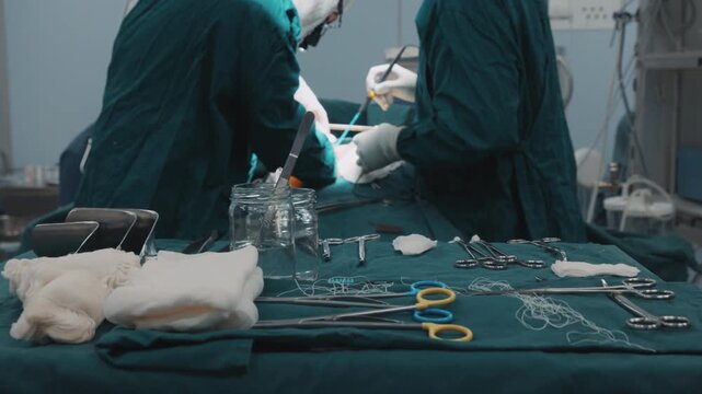 Surgeons performing a medical procedure in a hospital operating room while the patient lies on an operating table. Medical team in sterile uniforms working with surgical equipment in a controlled
