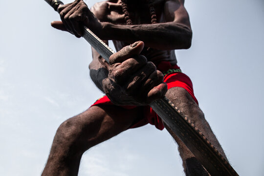 Sylhet, Bangladesh - 14 April 2025: View of a weathered ascetic's hands gripping a staff against the stark sky, vibrant red cloth a bold contrast to the muted tones of skin and wood.