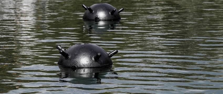 Two partially submerged mines with protruding parts in the dark water. 1908/1939 Soviet naval anchor mine.