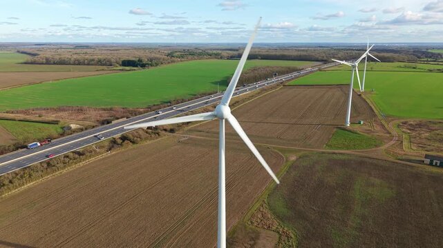 Cinematic panning aerial drone view of wind turbines near the M1 motorway in England during golden hour highlighting UK renewable energy infrastructure.